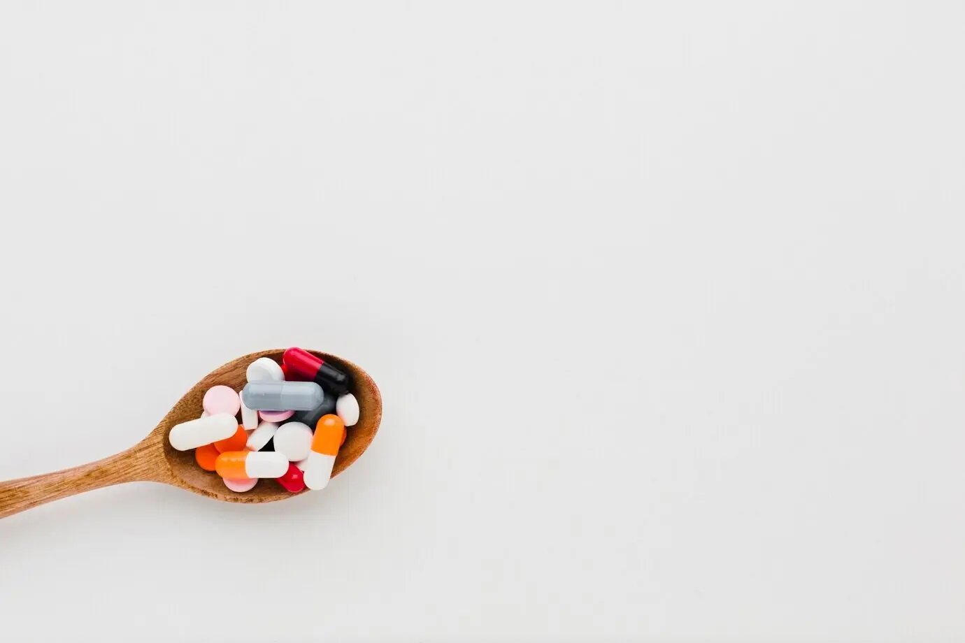 Вид сверху: деревянная ложка, наполненная таблетками, и свободное место для текста.